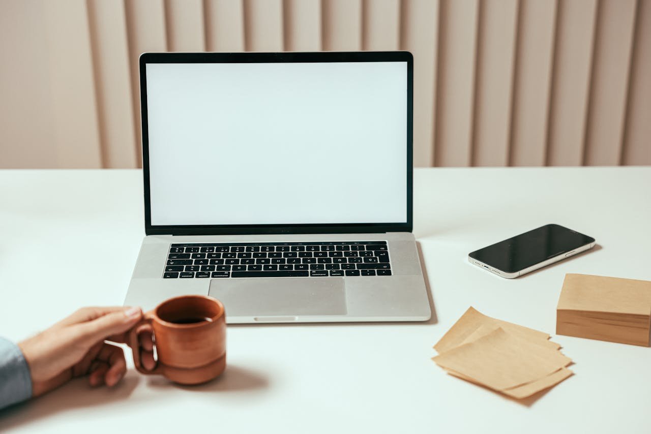 Minimalist workspace with laptop, smartphone, and coffee mug on a white desk.
